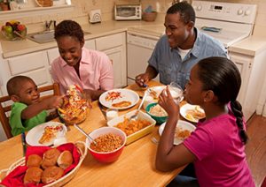 A family of four sits at a kitchen table to eat dinner.