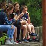 Teenagers sit on a wall eating snacks.