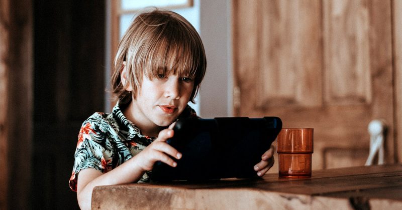 A young boy seated at a table using a tablet computer.