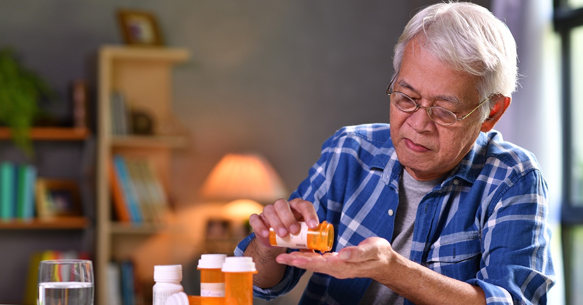 An elderly man pours a pill into his hand.