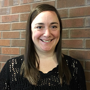 Laura Hooper in a black shirt smiling in front of a brick wall.