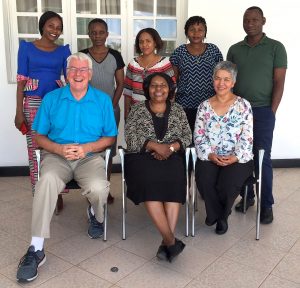 Simon Rosser and Zobeida Bonilla with six of their Tanzanian colleagues in front of a building.