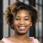 Shekinah Fashaw-Walters smiling in front of a bank of windows.