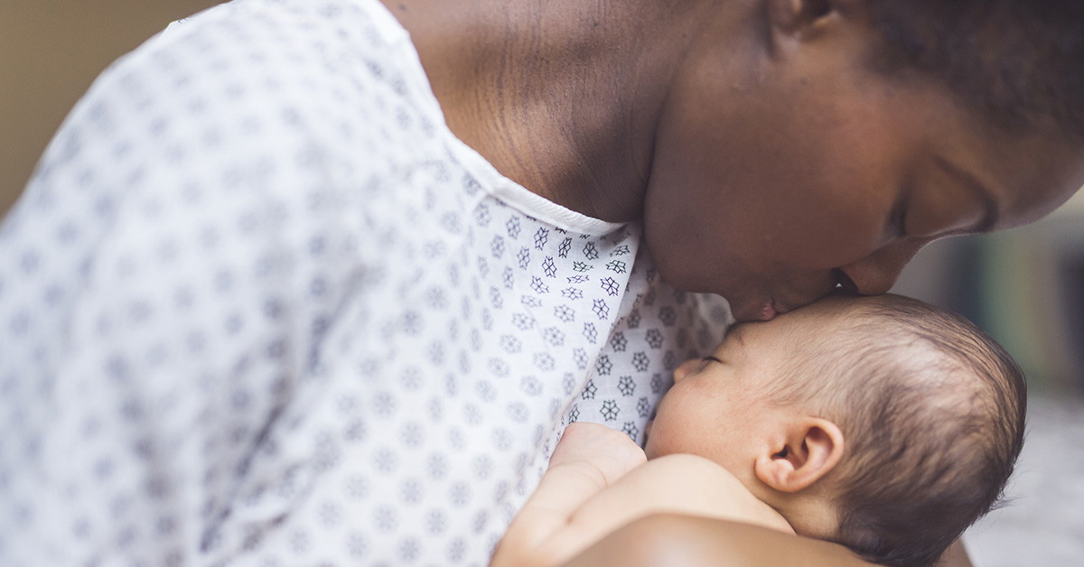 A Black mother dressed in a hospital gown kisses her newborn baby.