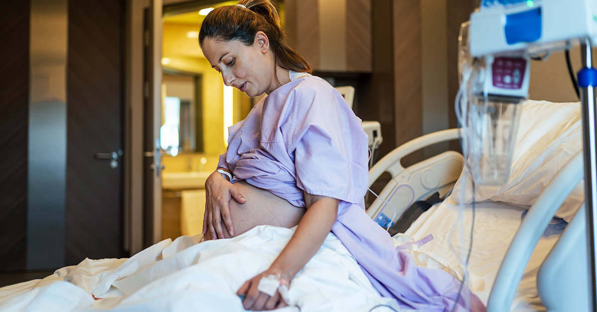 A pregnant woman sitting up in bed in a hospital obstetrics unit.