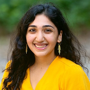 Shehrose Charania smiling while wearing a yellow top in front of a natural outside background.