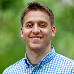 Cory Anderson smiling while wearing a blue and white dress shirt and standing outside.