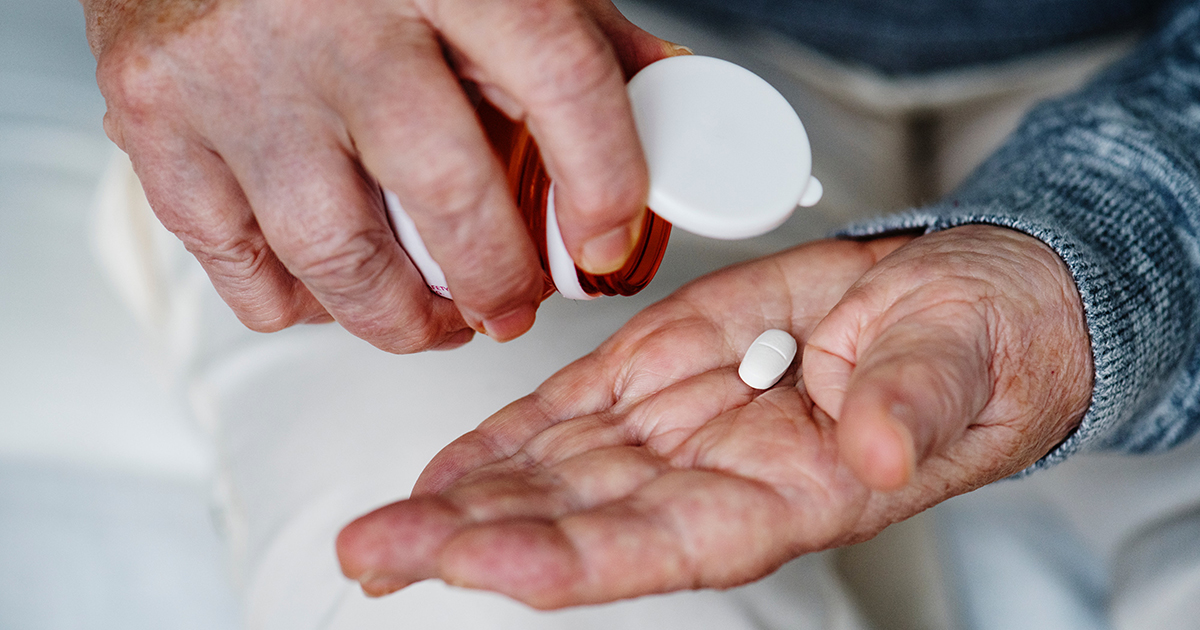 The hands of an elderly man holding a pill.