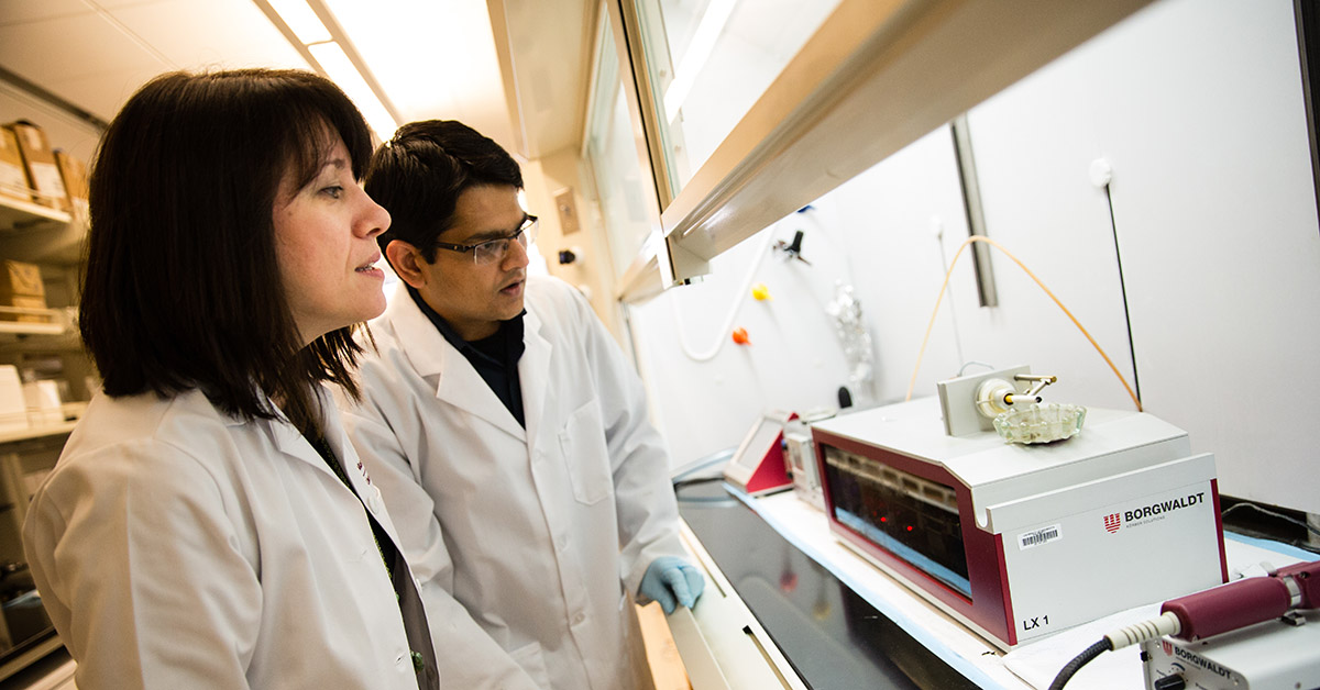 Two researchers watch a cigarette being burned using a smoking machine.