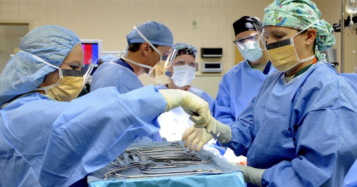 A surgical technician hands tools to a teammate.
