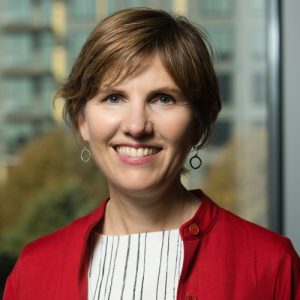 Susan Arnold wearing a red jacket and smiling in front of a window.