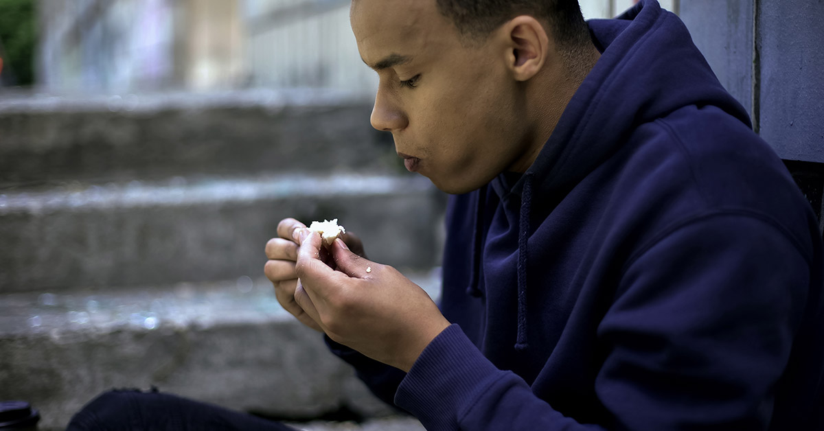 A teenage eating the last bite of a sandwich.