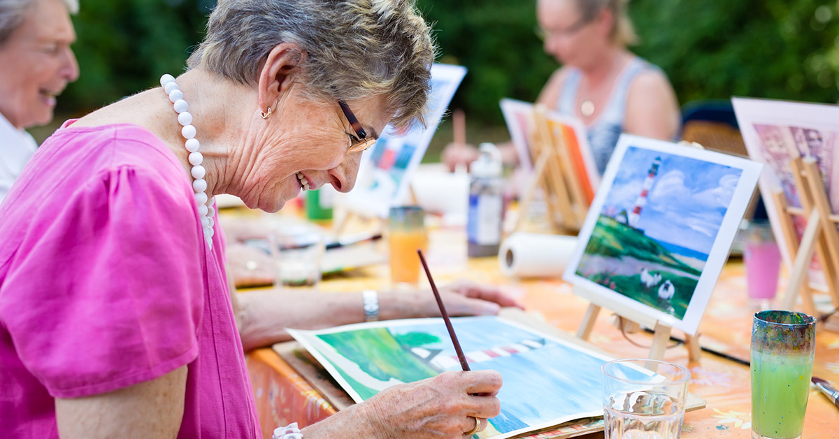 An older woman paints a picture during an art class.