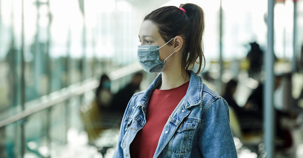 A young adult woman wearing a mask in public.