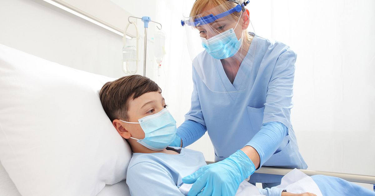 A female healthcare provider helps a boy laying in a hospital bed.