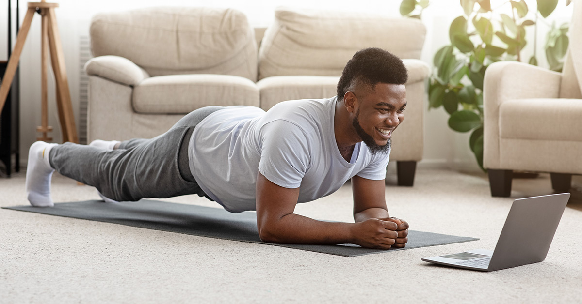 A young Black man practices yoga at home.