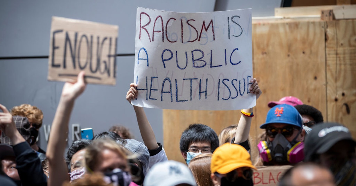In a crowd of protestors, a man holds a sign reading racism is a public health issue.