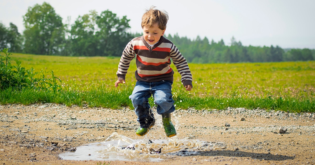 A boy jumps in a puddle in the middle of a country field.