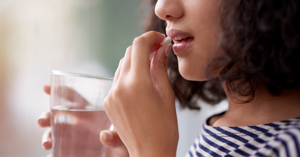 A young woman taking a pill with a glass of water.