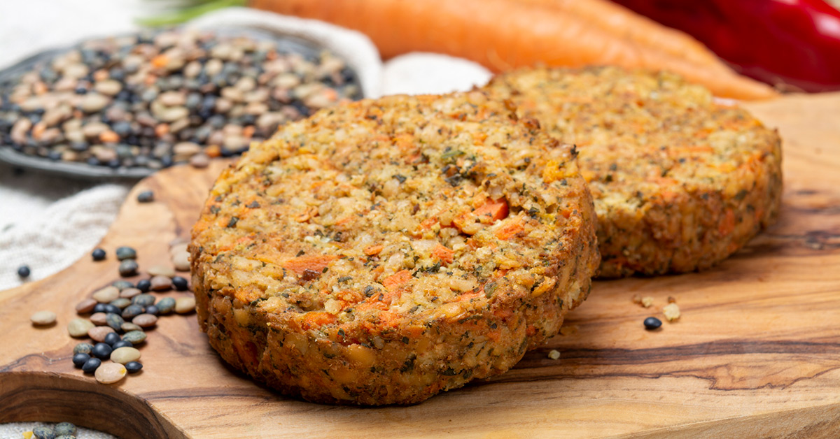 Two plant-based patties on a wood cutting board.