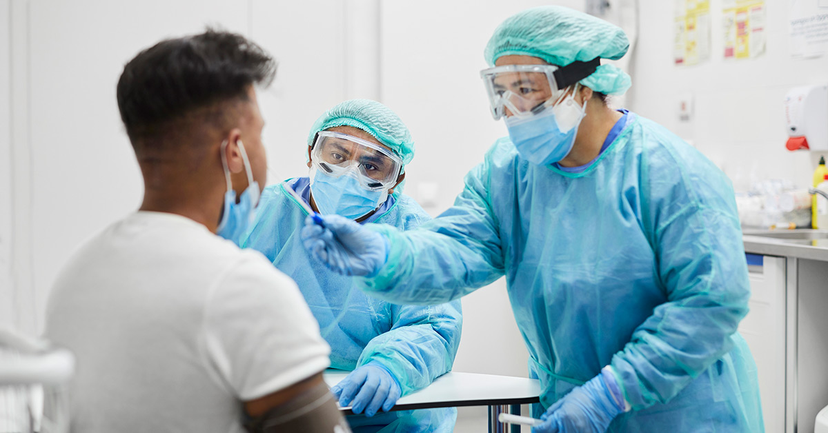 Two staff members in PPE test a patient for COVID-19.