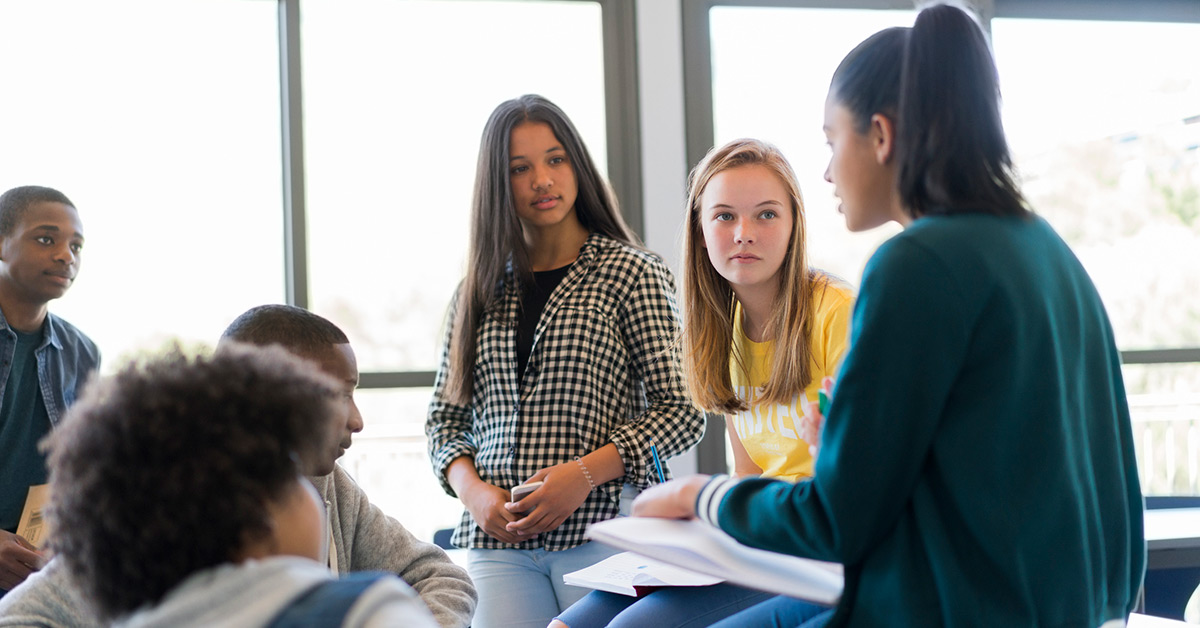 A group of teens talking in a classroom.