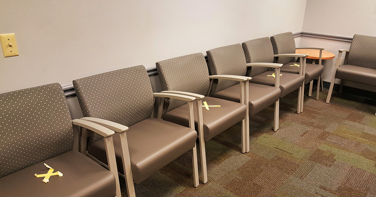 Empty chairs labeled for social distancing in a waiting room.