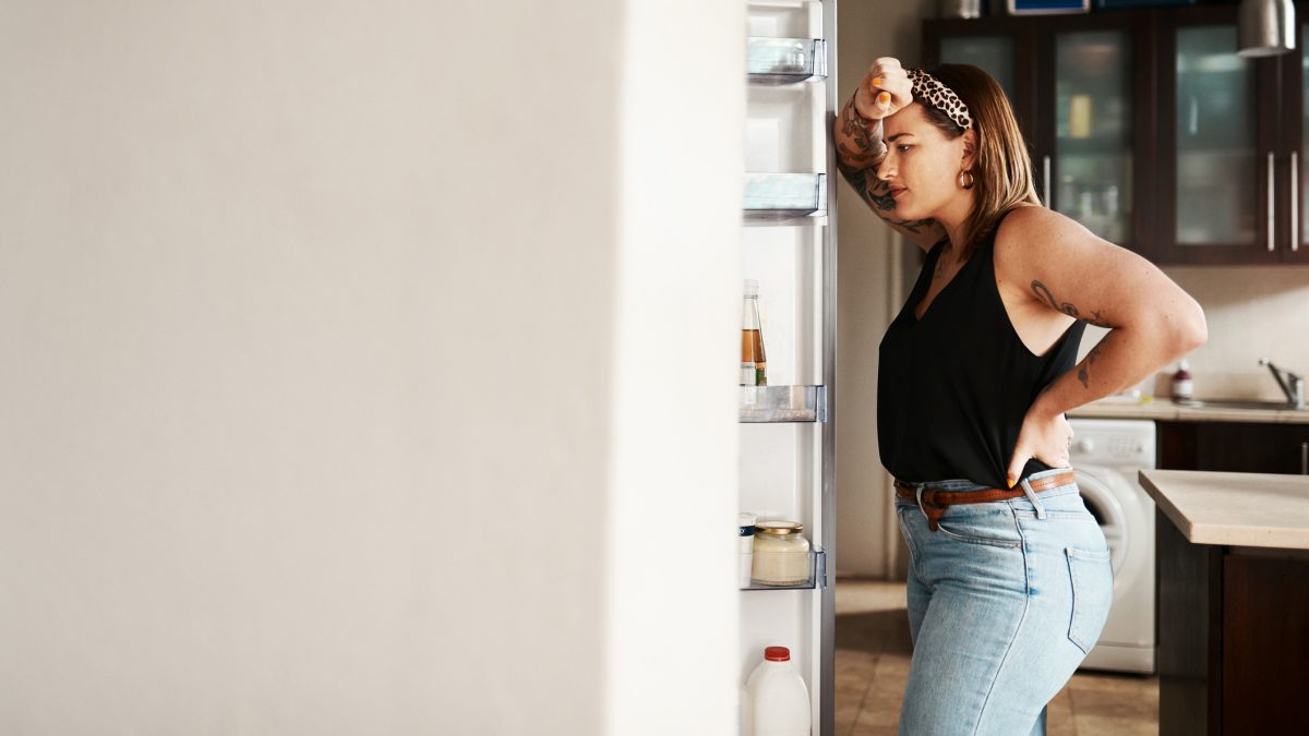 A woman in a black shirt and jeans looking into an open fridge.