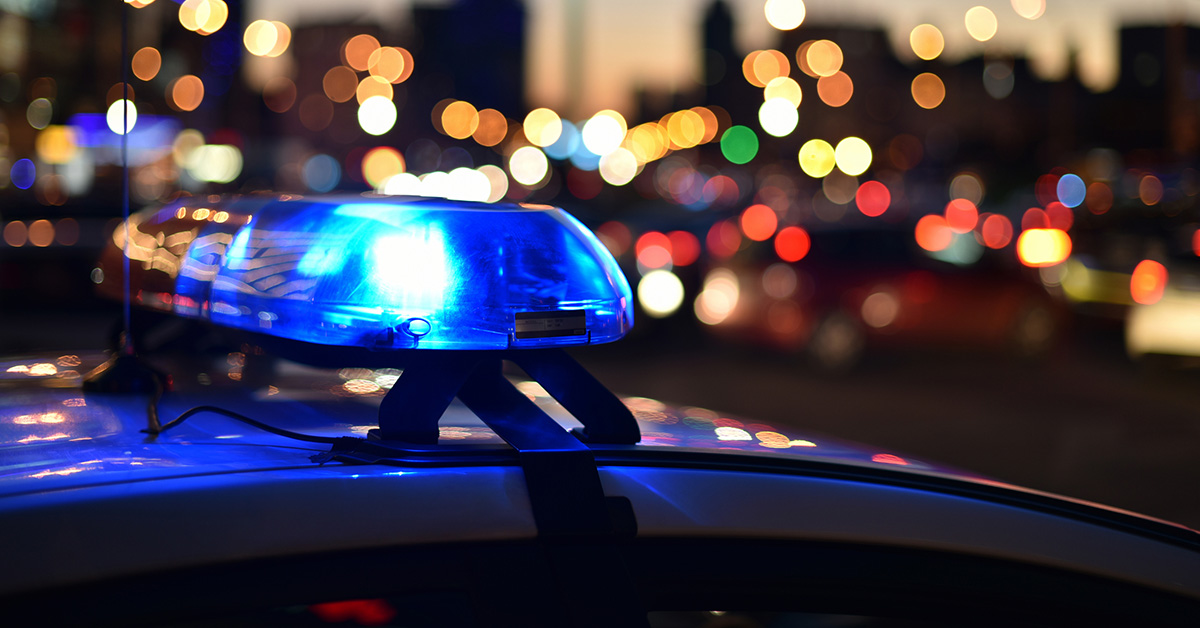 A blue light bar on top of a police car with a city street in the background.