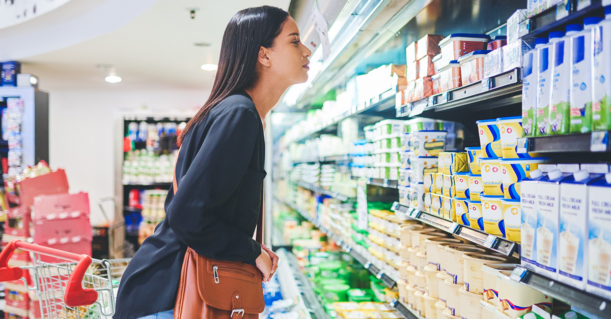 A woman grocery shopping surveys the choices of spreads in the dairy case.