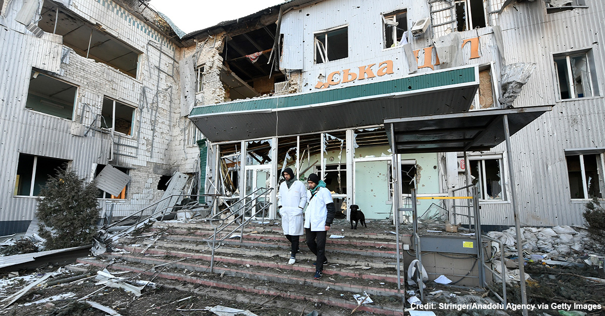 Workers walk down steps in front of a bombed-out Ukrainian hospital.