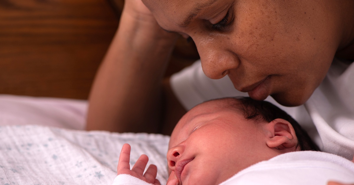 A Black mother nuzzling her baby in bed.