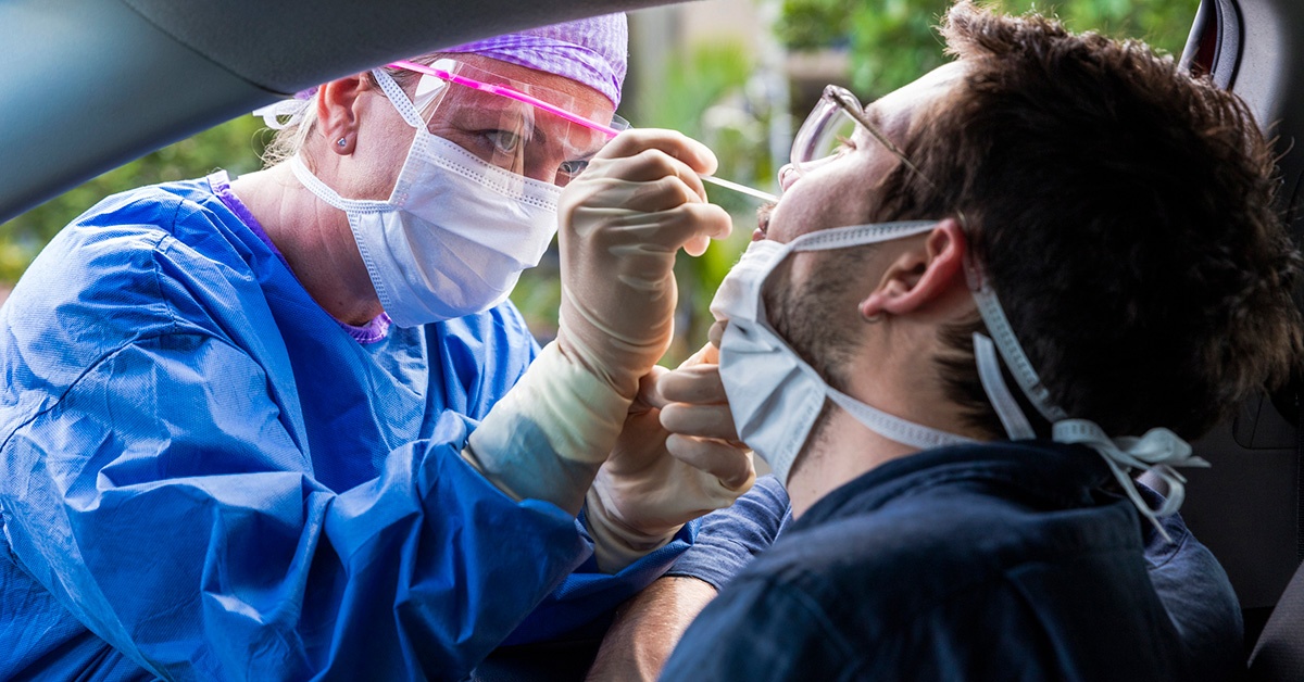 A health worker swabs the nose of a man seated inside a car.