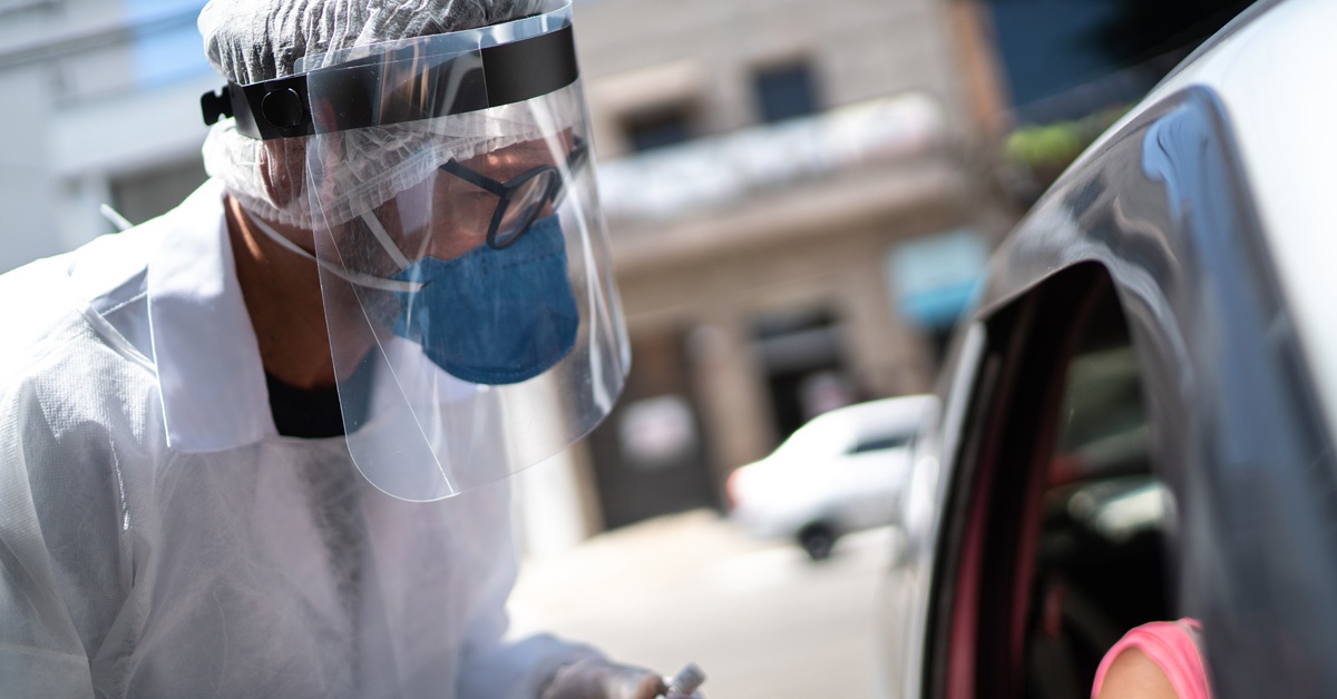 Healthcare worker in personal protective equipment talking to someone in a car