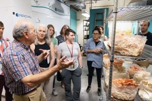 An instructor talks to students about giant, colorful fungi forms on a rack.