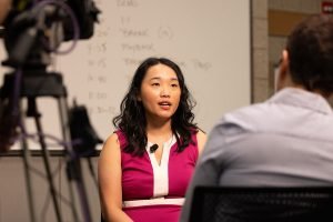 a woman looks at a man an an interview with a camera facing her.