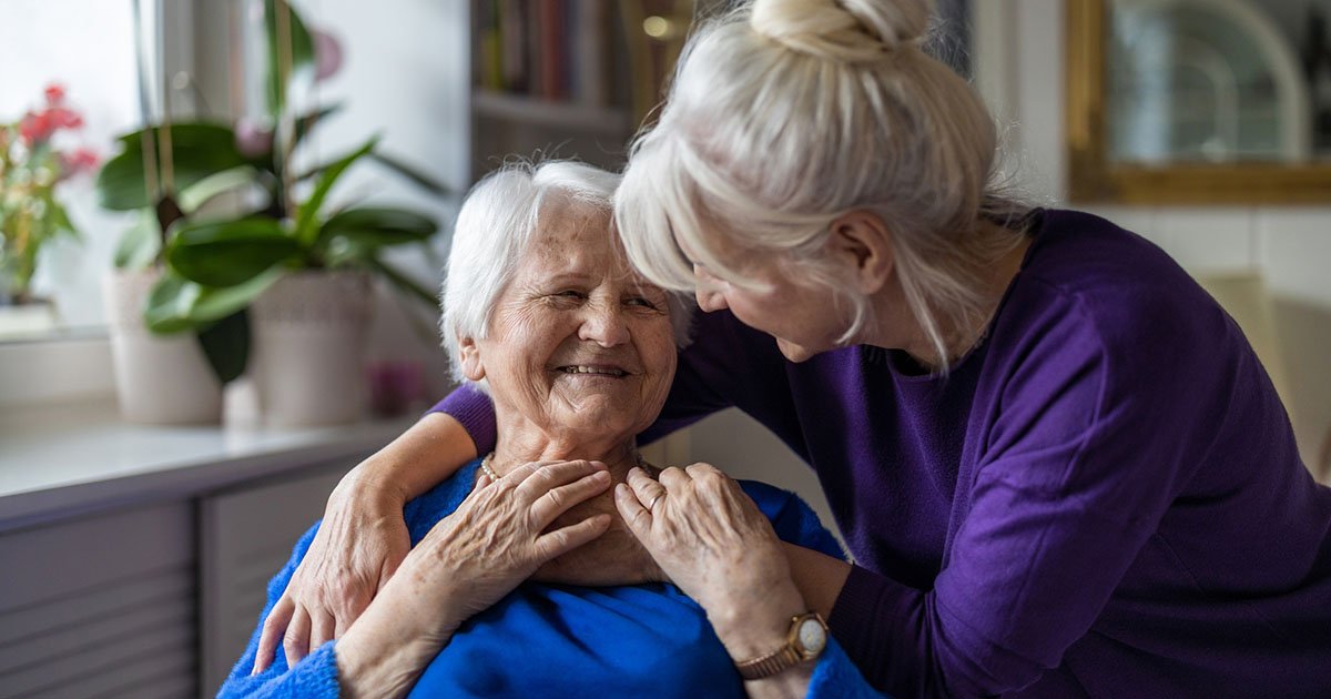 older woman in blue shirt is hugged by younger woman in purple shirt