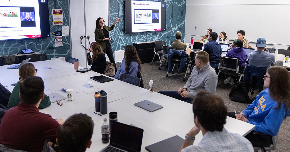 Paige Nong standing in a classroom standing and lecturing to students seated around tables