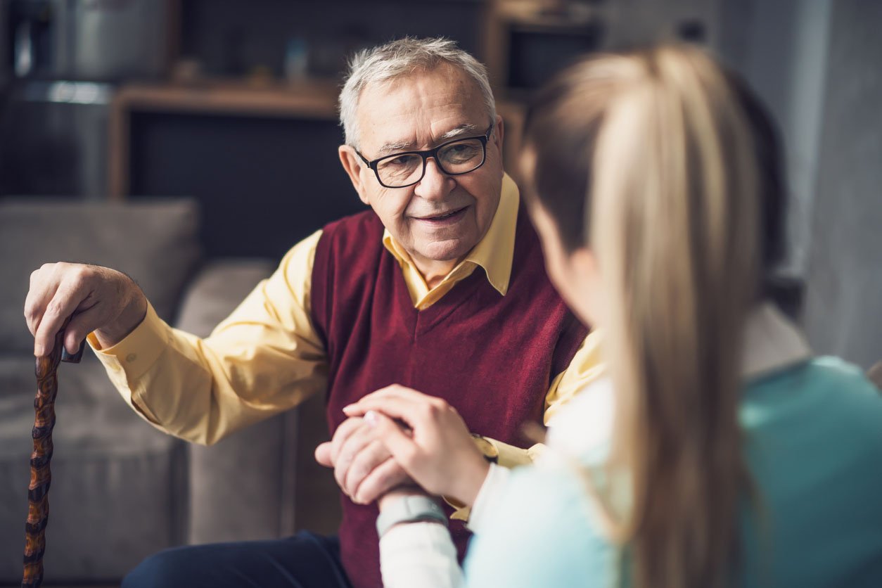 Female medical worker with back to the camera visits an older man holding a cane in a home medical visit