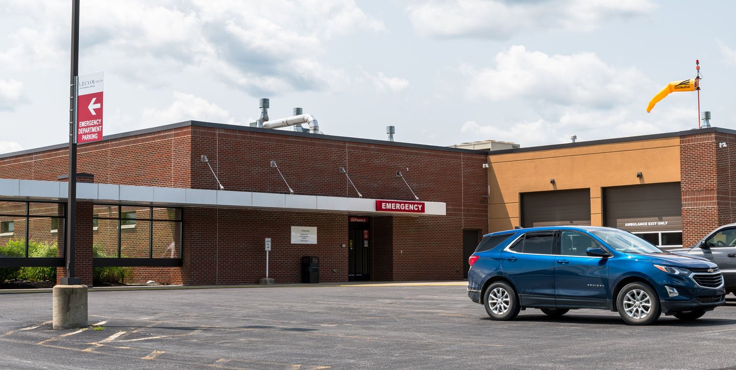Nearly empty parking lot of a small hospital with one car parked in it and a hospital building