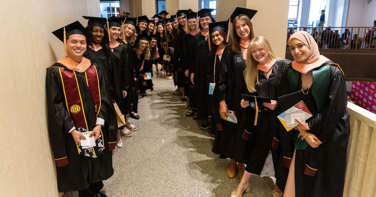 Several people in graduation robes and mortar board hats stand in a line