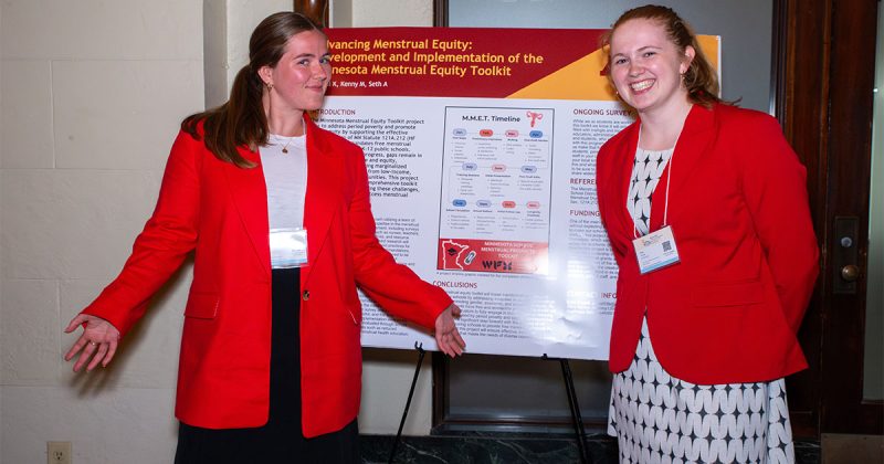 Mary Kenny and Kara Cowell stand in front of a poster about their research