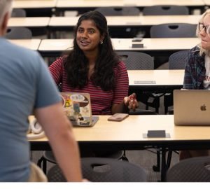 Seated female students speaking to a male professor in a classroom