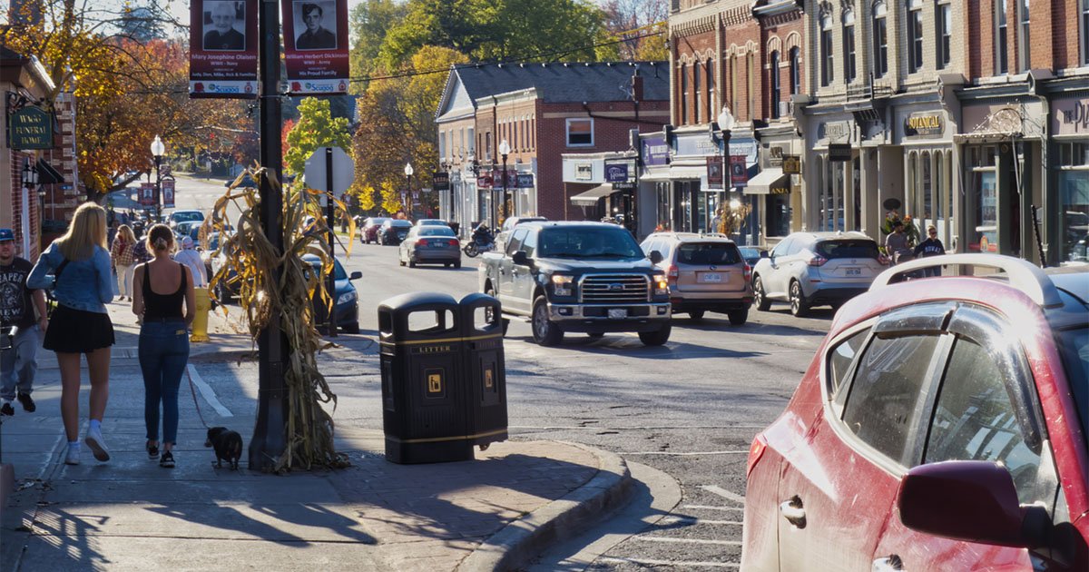 Small town main street with pedestrians along sidewalk and cars driving on the street
